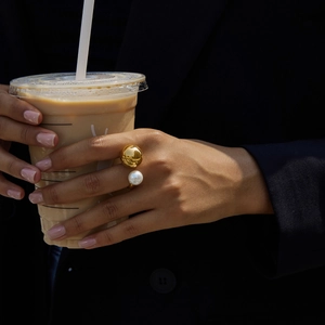 Close-up of gold tone ring with large white pearl on hand holding a coffee cup