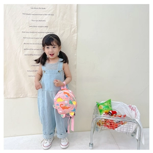 Pink backpack with dinosaur patterns held by a child model in a stylish studio