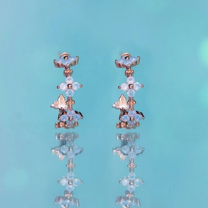 Macro detail of rose gold flower earrings with light blue opal and butterfly charms