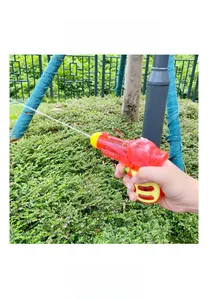 Outdoor shot of a mini red transparent water gun toy spraying a stream in a park