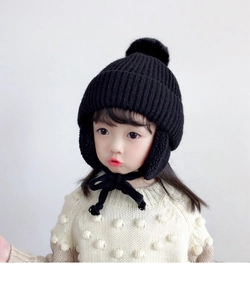 Detail of black knitted earflap hat for kids featuring soft pom-poms and secure straps