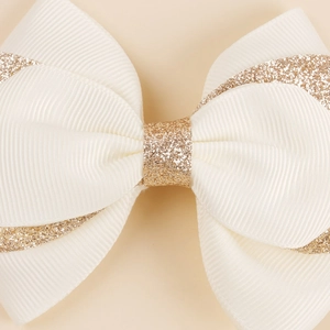 Detail of white grosgrain ribbon hair bow with elegant gold glitter edges and center