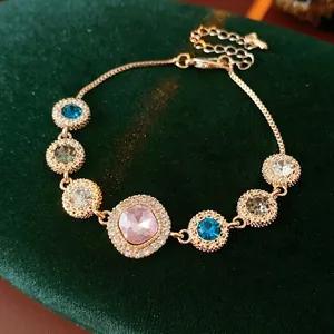 Elegant gold bracelet with multicolored round gems and pink centerpiece on green velvet