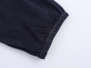 Dettaglio ravvicinato del denim blu scuro con cuciture arancioni e polsino con pieghe