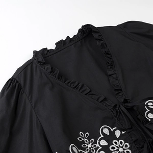 Close-up of the ruffled V-neck with white floral embroidery on a black elegant blouse