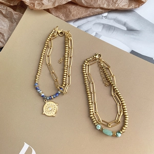 Detail of double-layer gold chain bracelet with blue beads and evil eye charm