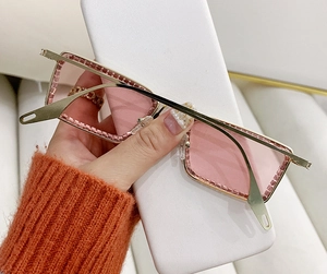 Detalle de gafas de sol cuadradas sin montura con lentes rosas y bordes de pedrería