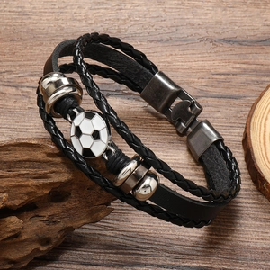 Detail of multi-layer braided leather bracelet with a soccer charm on rustic wood