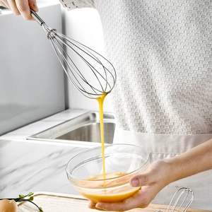 Manual stainless steel spring whisk mixing egg yolks into a glass bowl in a modern kitchen