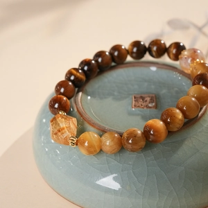 Macro detail of Tiger Eye beaded bracelet with citrine stone on a celadon ceramic plate