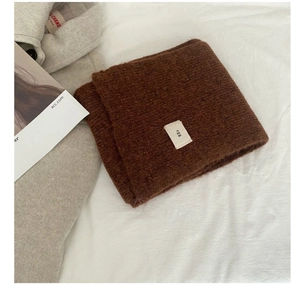 Close-up of dark brown wool blend scarf featuring minimalist white egg label detail