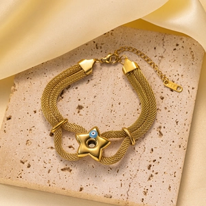 Detalle macro de la pulsera de malla multicapa con estrella dorada y dije de ojo azul