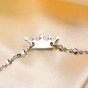 Close-up of silver stainless steel crown bracelet with heart-shaped chain on silk