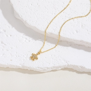 Macro shot of gold turtle pendant necklace with white zircons on white stone