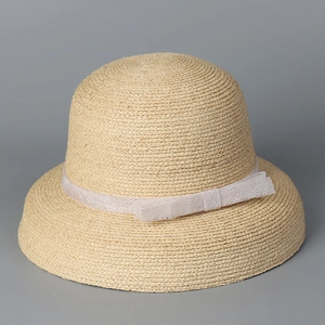 Detail of raffia straw hat with tight weave texture and delicate white lace bow detail