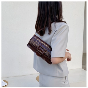 Side view of a dark brown crocodile pattern baguette bag worn on the shoulder by a model