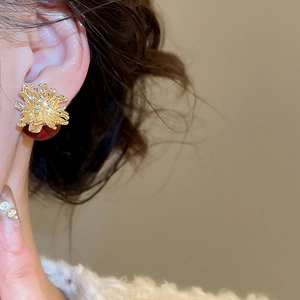 Macro side view of a gold firework earring with red pearl drop and crystal detailing