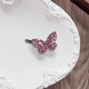 Close-up of a pink rhinestone butterfly hair clip on a textured white ceramic plate