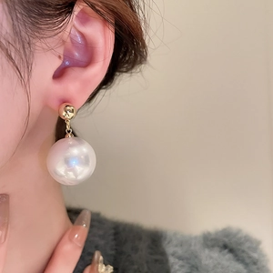 Close-up of elegant gold ball stud earrings with large white pearl drop on a model