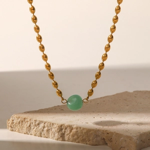 Close-up of a gold-plated oval bead chain necklace with a green natural stone pendant