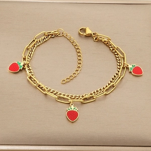 Detail of layered gold titanium chain bracelet featuring three red enamel strawberry charms