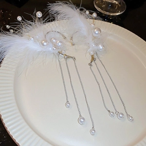 Detail of elegant feather and pearl tassel ear cuffs on a white textured plate