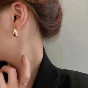 Close-up of minimalist golden C-shaped bean earrings and matching ring on a model