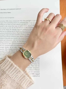 Close-up of a women's square green dial watch with gold steel strap and fashion rings