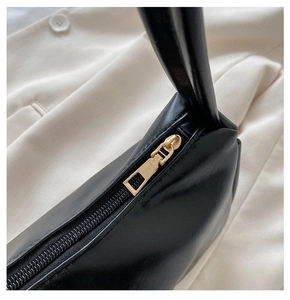 Close-up of smooth gold zipper and fine leather texture on minimalist black underarm bag