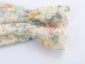 Detailed macro view of French-style floral embroidery and wavy ruffle hem on white cotton shirt