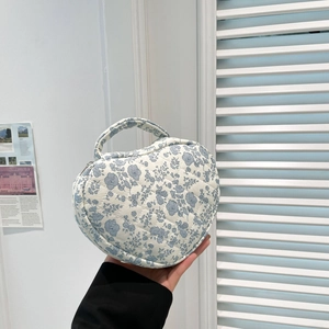 Handheld view of a heart-shaped quilted makeup bag with blue floral patterns and zip closure