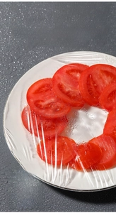 Macro shot of thick food-grade PE elastic cling film covering fresh tomato slices