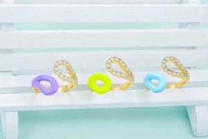 Detailed shot of three colorful enamel gold open rings with zircons on a white bench