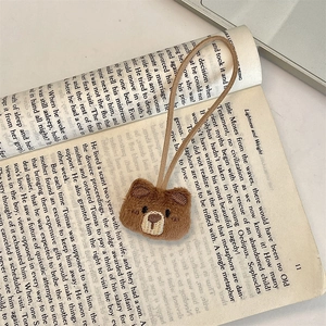 Detail of cute brown plush bear charm with khaki suede strap on an open book