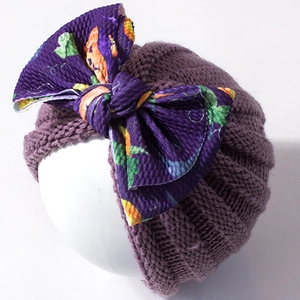 Detail of warm dark purple baby knit hat with a large Halloween pumpkin pattern bow