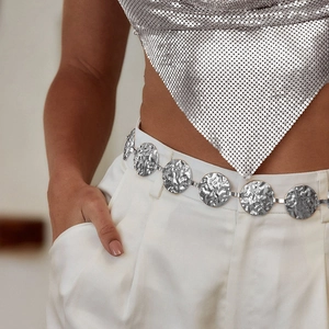 Detailed macro view of silver hammered metal circle waist chain on model with white pants