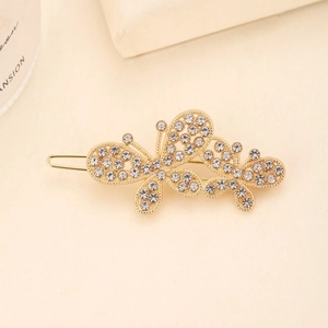 Close-up of golden hollow butterfly hair clip with rhinestones and pearls on beige background