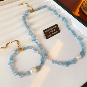 Macro detail of 925 silver jewelry set with light blue stones and white pearls on white tray