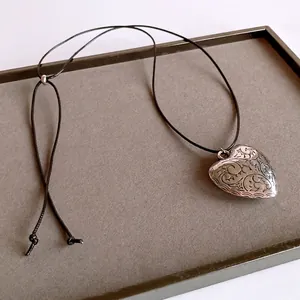 Vintage engraved heart pendant necklace with adjustable black wax cord on a plush display