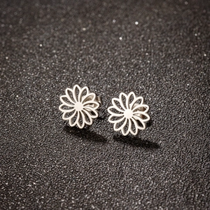 Detailed macro view of silver hollow daisy floral stud earrings on a dark sparkling surface