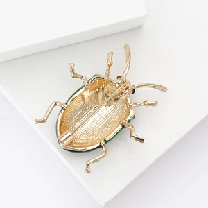 Macro detail of the golden beetle brooch showing the secure metal pin clasp and texture