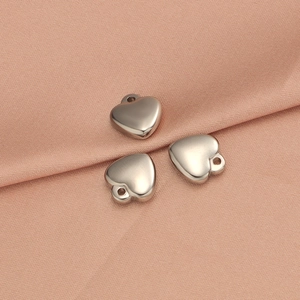 Close-up of three polished silver heart charms on pink silk for DIY jewelry