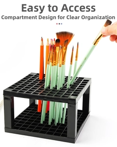 Detail of 96-slot black plastic paintbrush holder showing square grid and hand inserting brush