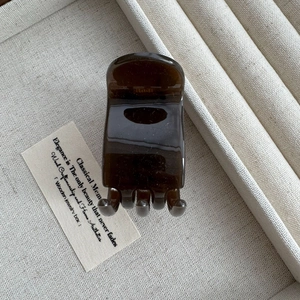 Close-up of a 5cm dark amber glossy hair claw clip on a beige linen jewelry tray