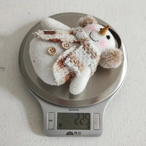 Detail shot showing a 22.5g lightweight plush snowman hanging ornament on a scale