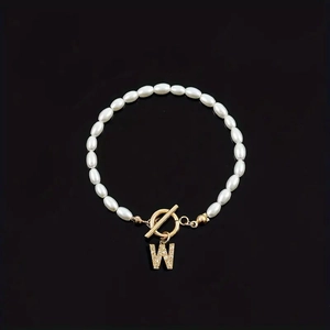Faux pearl beaded bracelet with gold-tone rhinestone initial charm on black background