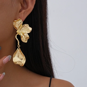 Macro shot of large golden metallic flower earrings with intricate petal textures on model