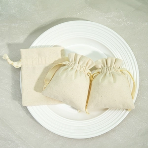 Three beige cotton linen jewelry pouches presented on a white plate with soft lighting