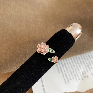 Macro d'une bague ouverte dorée à l'or 14K avec des pétales de rose roses et feuilles vertes