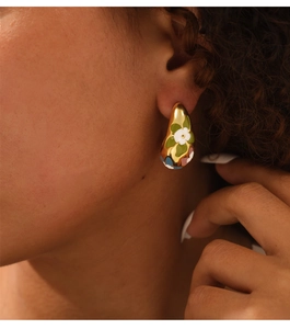 Detailed view of C-shaped gold-plated titanium earrings with floral enamel pattern on model